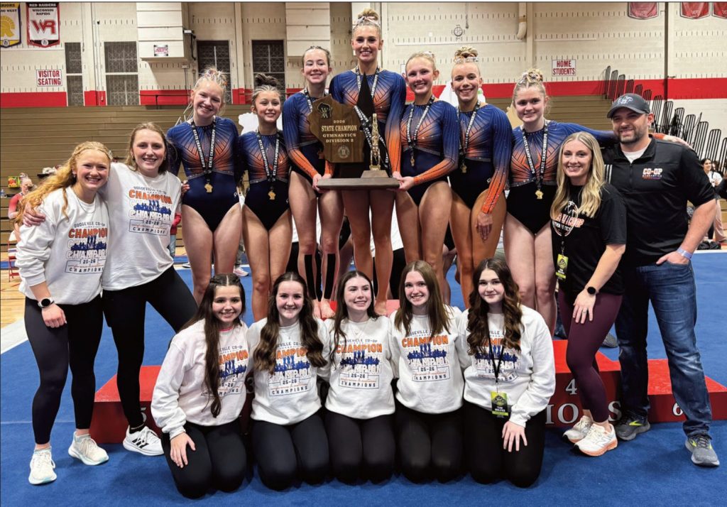 The Dodgeville Co-Op Gymnastics Team stands on the podium with its WIAA Division 2 State Championship trophy.